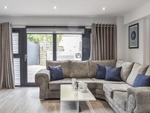 Un salon moderne avec un canapé d’angle, une table basse et une vue sur l’extérieur, accessible par une porte vitrée.