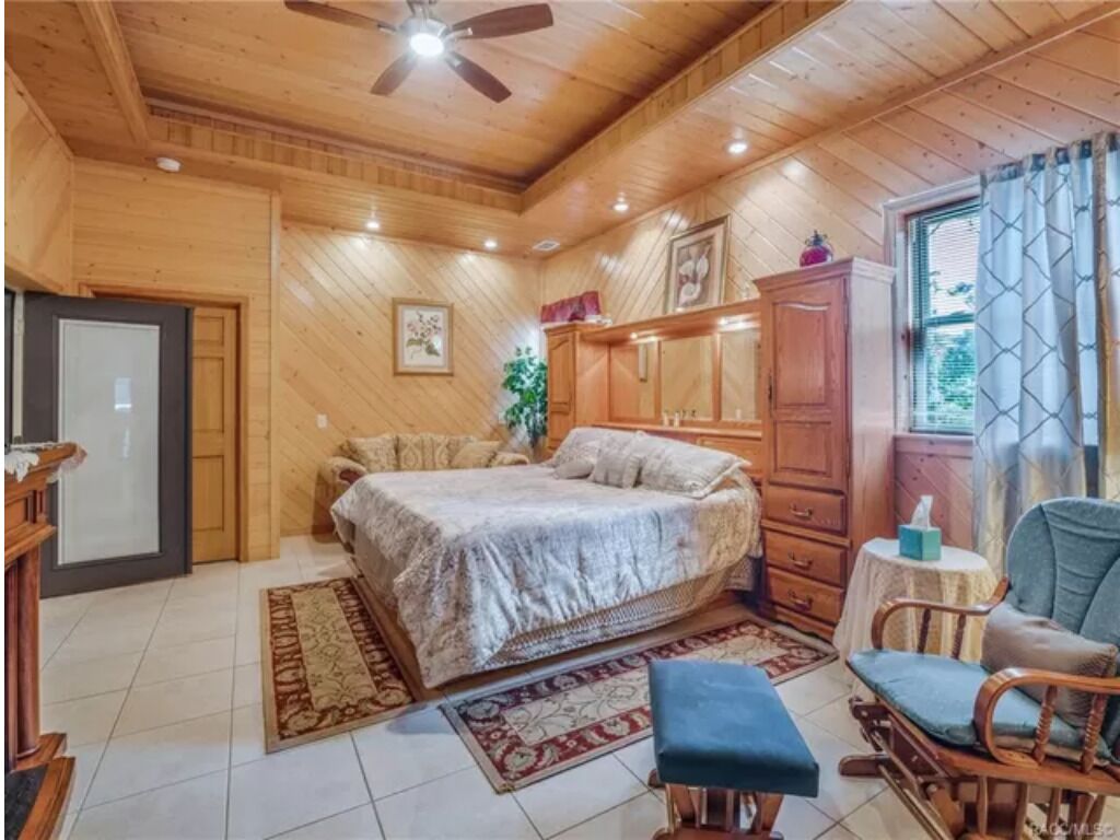 Ein Schlafzimmer mit Holzwandverkleidung, einem Bett, einem Schreibtisch, einem Stuhl und einem Fenster mit Vorhängen.