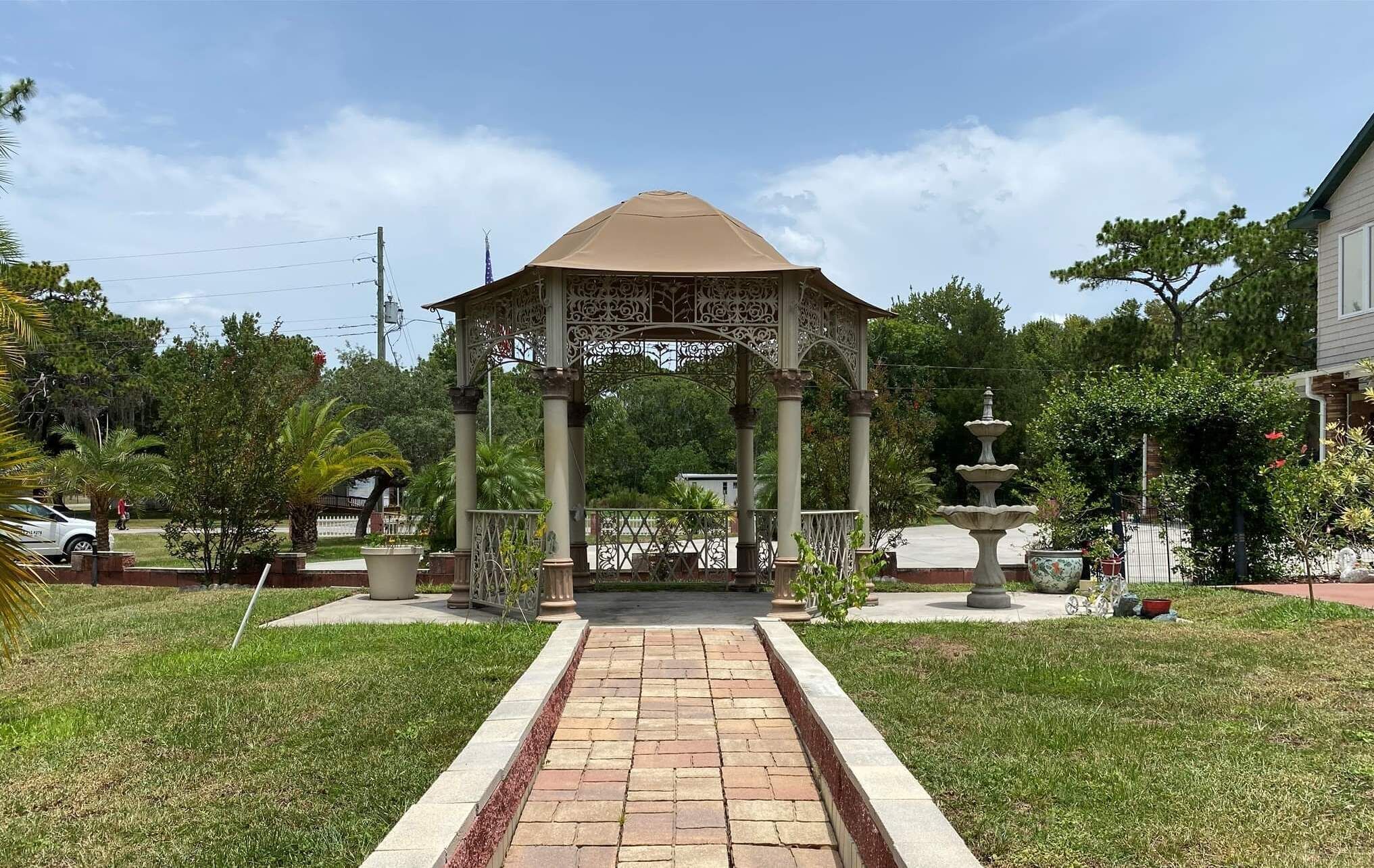 Ein Pavillon mit einem mit Fliesen belegten Weg, umgeben von Grünpflanzen und einem Brunnen.