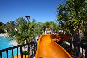 A water slide at a resort with a pool and palm trees.