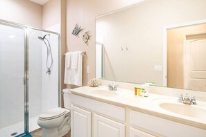 A bathroom with a glass shower enclosure, a toilet, a double sink vanity, and a large mirror.
