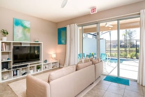 A living room with a TV, sofa, and a view of a pool.