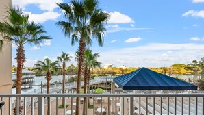 A terrace with outdoor seating, palm trees, and a view of a body of water and distant buildings. - Laketown Wharf Unit 104 (Panama City Beach)