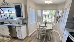 A modern kitchen with a dining area, wooden flooring, white cabinetry, and a window with blinds. - 5 star resort 4 bedroom, 3 bath,heated pool/spa, putting green,7 flat screen tvs (Peoria)