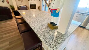 A modern kitchen with a granite countertop, a large white statue of a chef, and a dining area with a sofa and chairs. - 5 star resort 4 bedroom, 3 bath,heated pool/spa, putting green,7 flat screen tvs (Peoria)