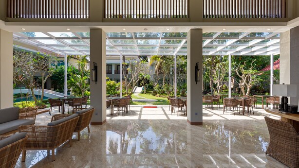 A spacious indoor area with a glass ceiling, wicker furniture, and a view of a garden and pool. - THE GANTARI UBUD HOTEL & VILLA (Ubud)