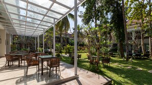 A covered outdoor area with wooden flooring, tables, and chairs, surrounded by lush greenery and trees. - THE GANTARI UBUD HOTEL & VILLA (Ubud)