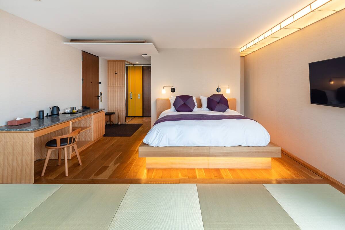 A modern hotel room with a wooden bed, a desk, and a television.