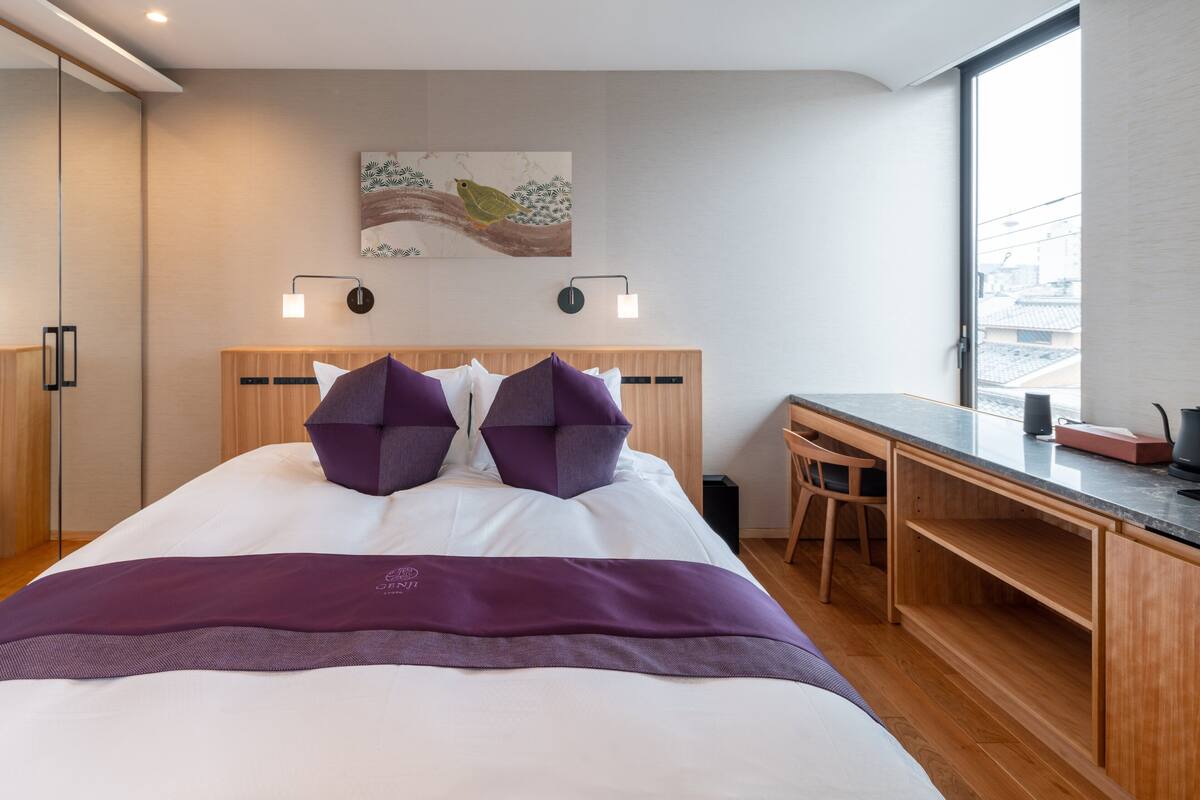 A modern hotel room with a large bed, a desk, and a view of the city.