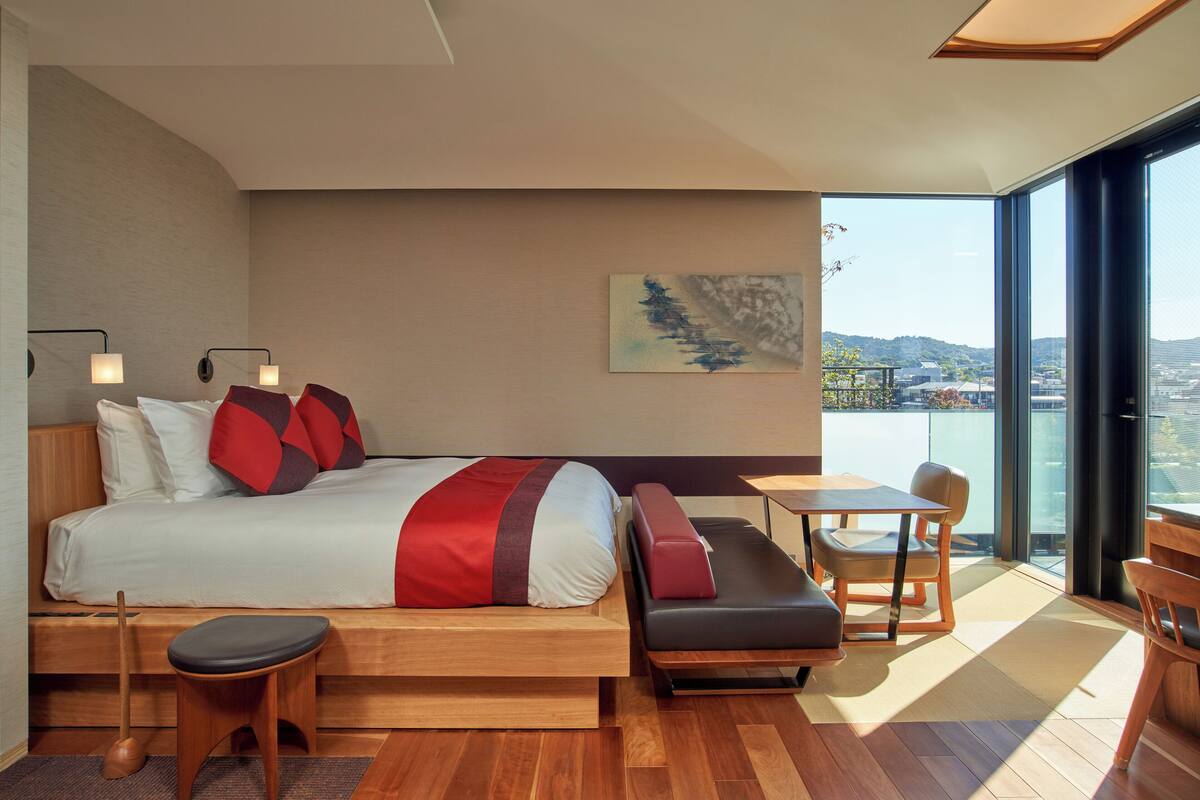 A modern hotel room with a large bed, a seating area, a small table, and a view of the city.