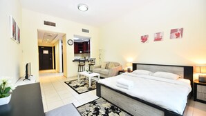 A hotel room with a large bed, a desk, a chair, a sofa, and a small table. There is a clock on the wall and a window with curtains. - KEN - Spectacular Furnished Studio (Dubai)