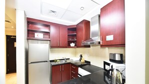 A modern kitchen with dark wood cabinets, stainless steel appliances, and a black countertop. - KEN - Spectacular Furnished Studio (Dubai)