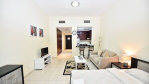 A modern hotel room with a bed, a TV, a desk, a chair, a sofa, and a kitchen area in the background. - KEN - Spectacular Furnished Studio (Dubai)
