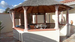 A covered outdoor dining area with a thatched roof, wooden pillars, and a tiled floor. - Villa Carthage confort & vue piscine XL / Downhill stylish Villa view & XL pool (Calignac)