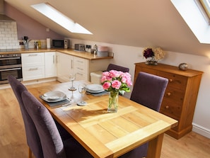 A dining area with a wooden table, purple chairs, a vase with pink flowers, and a kitchen in the background. - 1 bedroom accommodation in Askwith, near Ilkley (Askwith, near Ilkley)