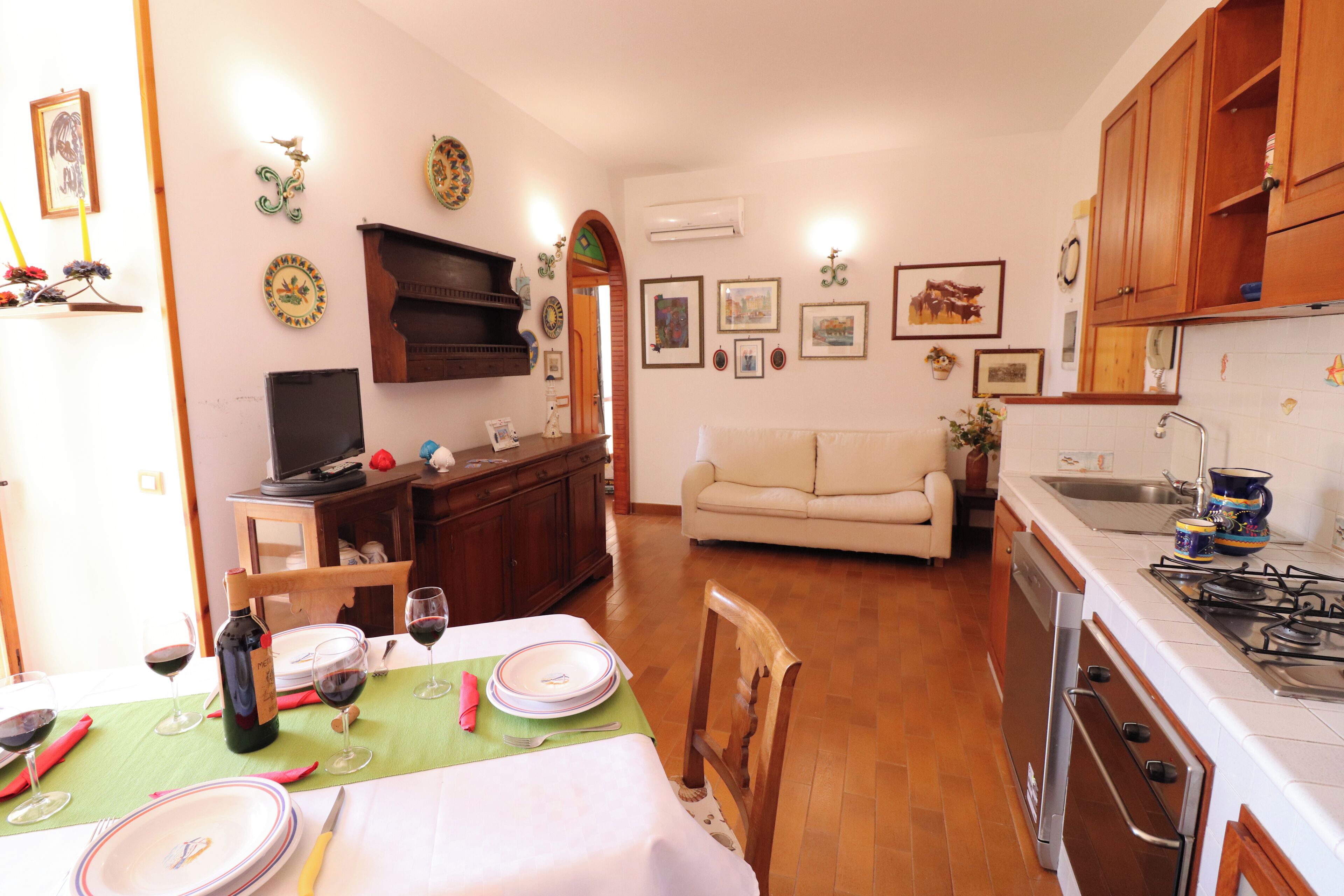 Un comedor con una mesa dispuesta para dos personas, un sofá y una cocina con armarios de madera y una estufa.