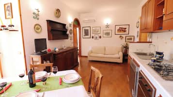 Un comedor con una mesa dispuesta para dos personas, un sofá y una cocina con armarios de madera y una estufa.