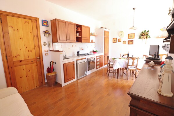 A kitchen with wooden cabinets, a dining table, chairs, and a refrigerator.