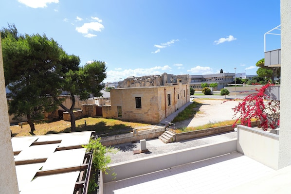 A courtyard with a stone building, a tree, and a red flowering plant.
