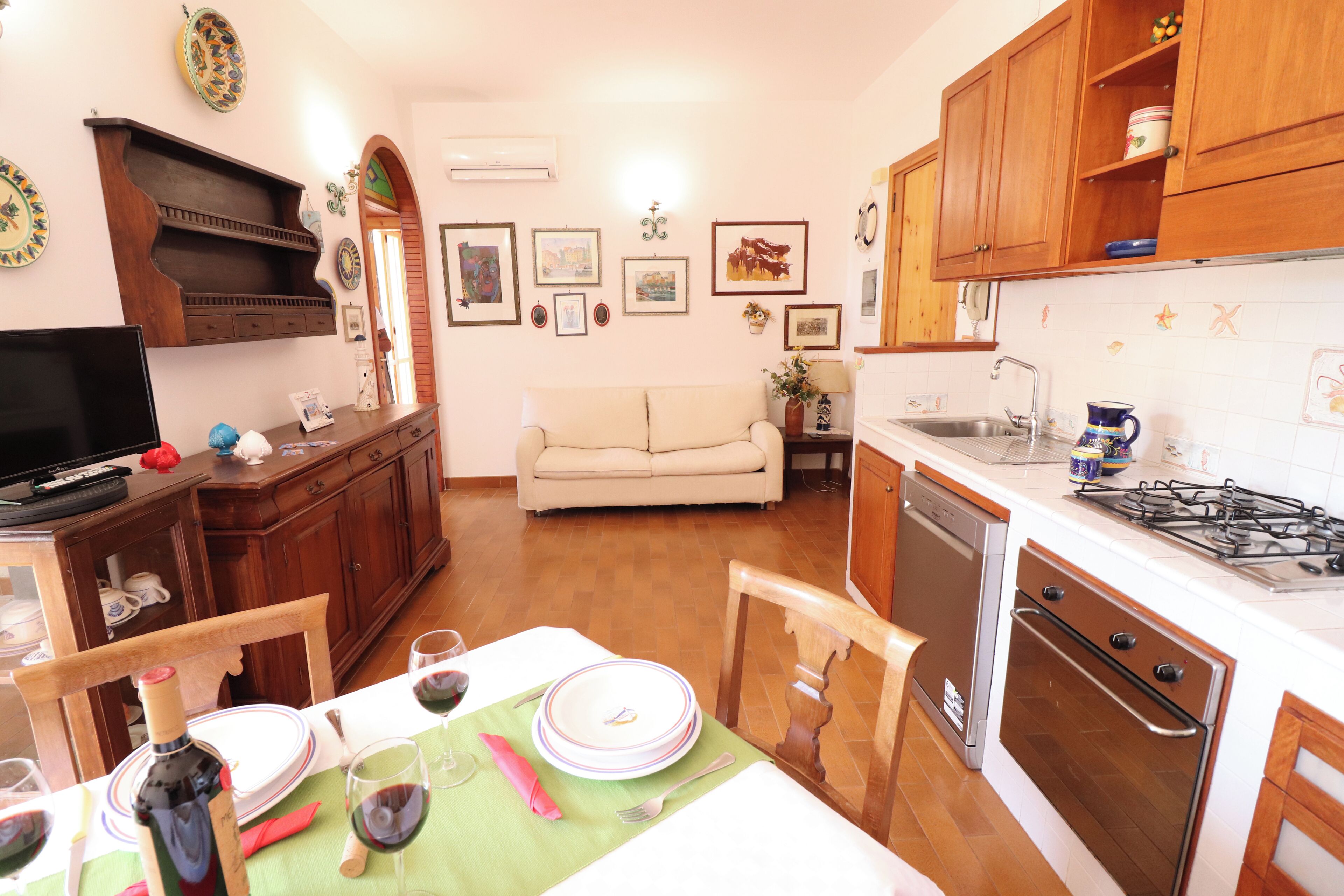 Una cocina con armarios de madera, una mesa de comedor preparada para cuatro personas y un sofá en la sala de estar.