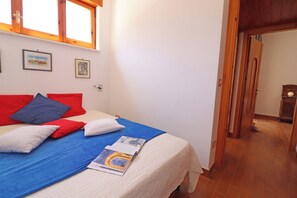 A bedroom with a bed, pillows, a magazine, a window, and a door leading to another room.