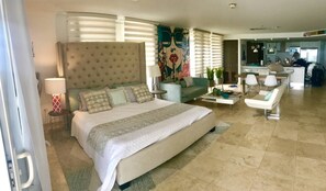 A hotel room with a large bed, a sofa, a coffee table, and a dining area.