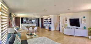 A modern living room with a sofa, coffee table, TV, and a dining area with chairs and a table.