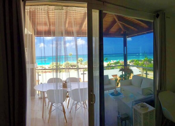 A balcony with a view of the ocean, a dining area with chairs, and a sofa.
