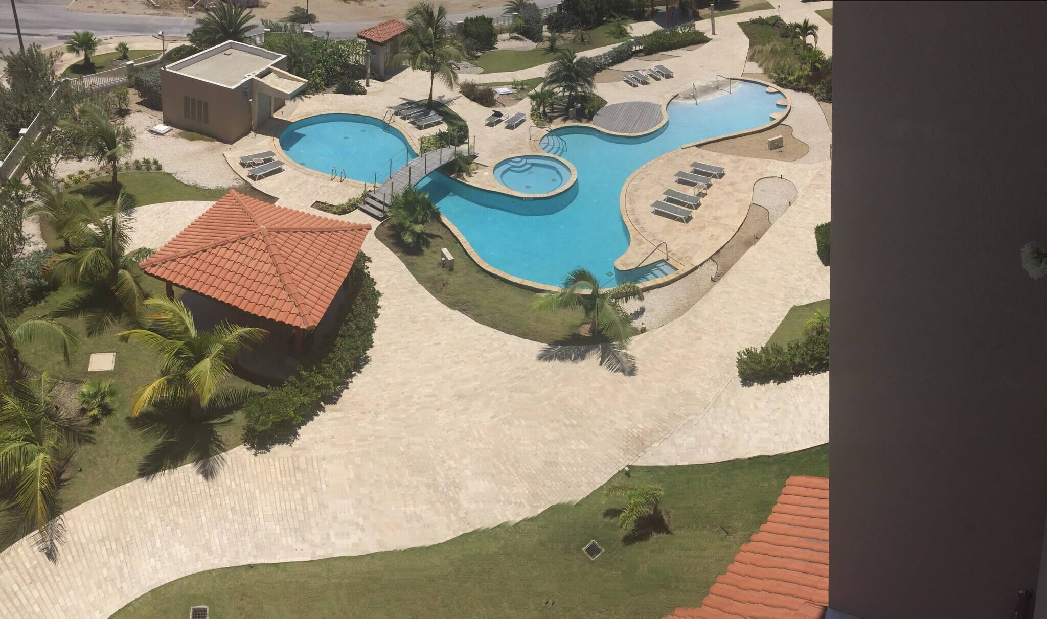 A resort with a large swimming pool, palm trees, and a red-roofed building.