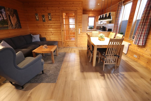 Cozy cabin-style room with a comfortable sofa, dining area, and wooden paneling.
