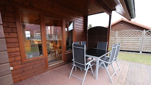 Une cabane en bois dotée d’un patio comprenant une table et des chaises, une porte-fenêtre coulissante et un sol en briques.