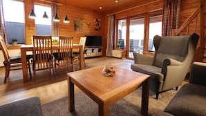 L’intérieur d’un chalet en bois chaleureux et accueillant, avec un coin repas, un canapé et un téléviseur.