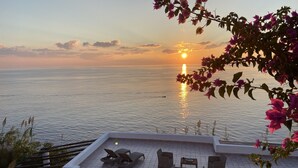 A terrace with a view of the sea at sunset, featuring a seating area with lounge chairs and a table. - Villa "mare" - Suspended Over the sea (Lipari)