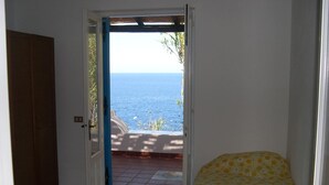 A bedroom with a bed, a bathroom door, and a view of the sea through an open door. - Villa "mare" - Suspended Over the sea (Lipari)