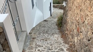 A narrow stone pathway leading to a white building with a metal gate. - Villa "mare" - Suspended Over the sea (Lipari)