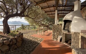 An outdoor patio with stone flooring, a rustic stone oven, and a view of a lake with mountains in the background.