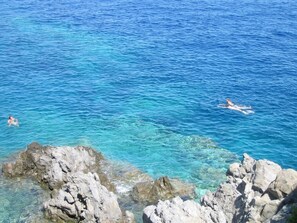 A coastal scene with clear blue water, rocky outcrops, and swimmers.