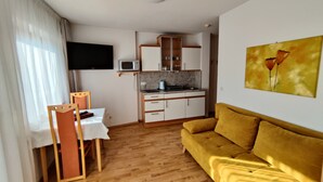 A compact living space with a kitchenette, a sofa, a dining area, and a TV mounted on the wall. - Residence Klementhof (Naz Sciaves)