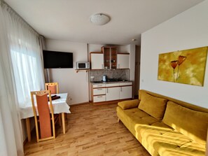 A compact living space with a kitchenette, a sofa, a TV, and a painting.