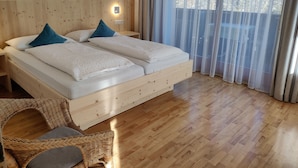 A wooden bed with two pillows, a nightstand, a wicker chair, and a window with sheer curtains. - Residence Klementhof (Naz Sciaves)
