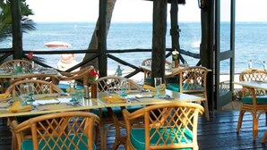 Un área de comedor al aire libre con sillas y mesas de mimbre, con vista al mar.