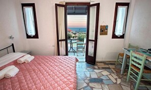 A bedroom with a bed, a small table, and a view of the sea through an open door. - Studio With sea View, Creta, Ierapetra (Ierapetra)