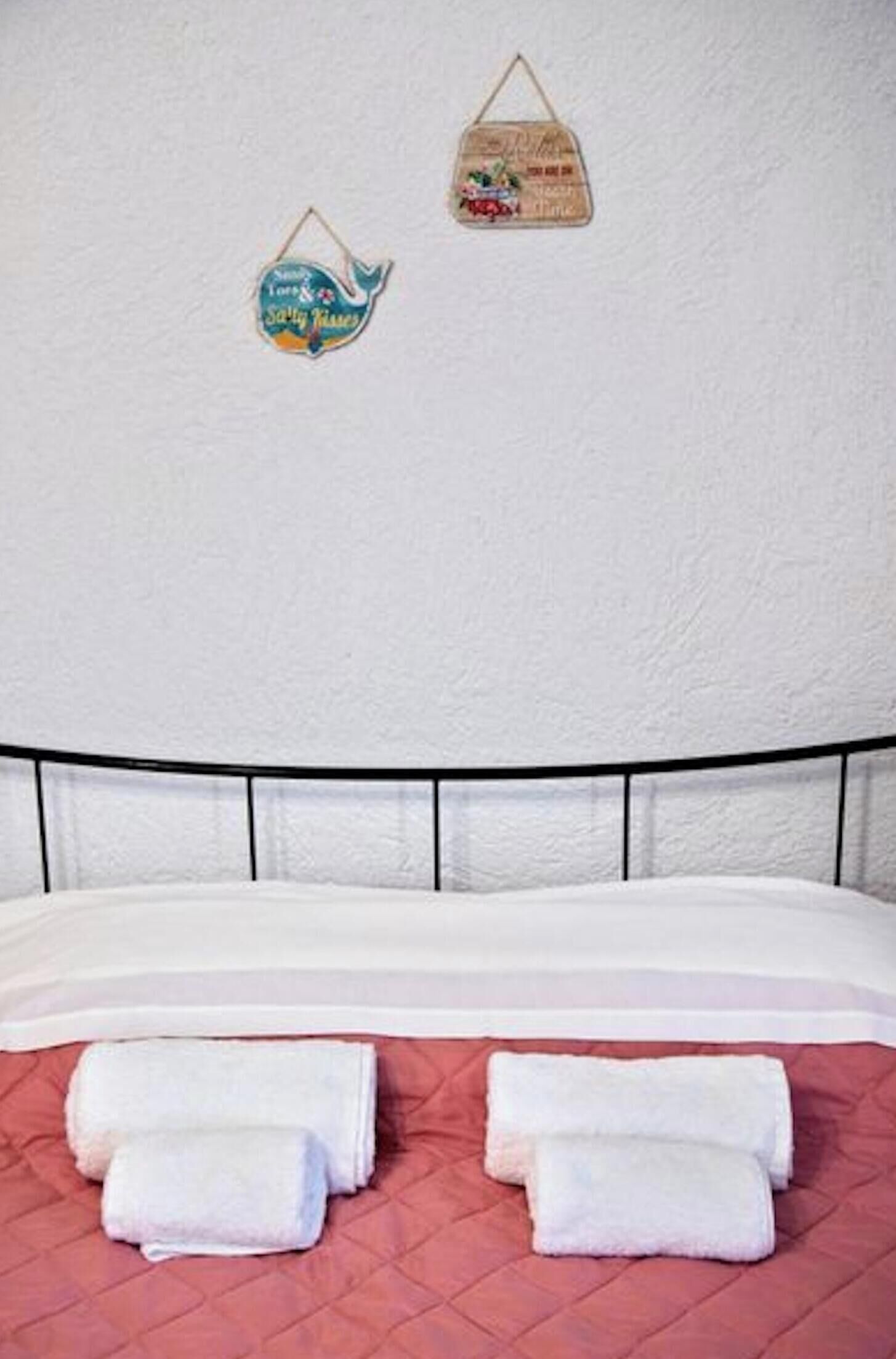 A bed with white linens and rolled towels, a black headboard, and two wall decorations.