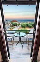 Ein offener Balkon mit Tisch und Stühlen, der auf eine Küstenlandschaft mit Gebäuden und viel Grün blickt.