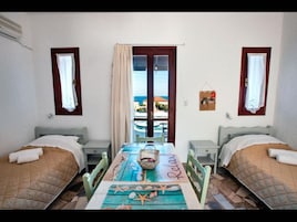 Ein Zimmer mit zwei Betten, einem Tisch mit einem Küsten-Tischläufer und Blick auf das Meer durch ein Fenster.