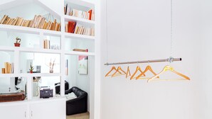 Una habitación con una estantería blanca, un sofá de cuero negro y un perchero con perchas.