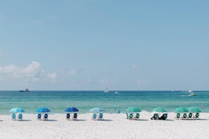 Una spiaggia con file di sedie a sdraio e ombrelloni, cielo sereno e barche sull'acqua.