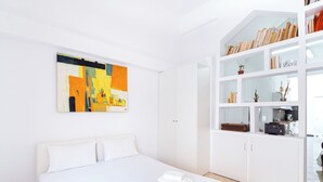 Una habitación de hotel moderna con una cama grande, un armario blanco y un cuadro abstracto y colorido en la pared.