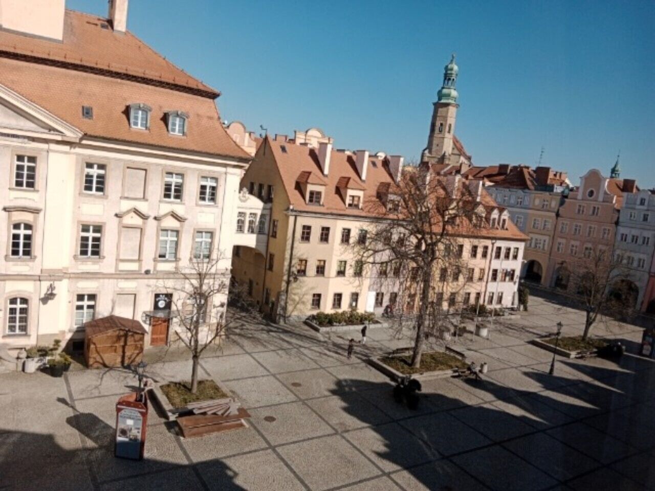 A square with buildings, a clock, and a small tree.