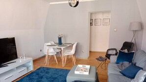 A modern living room with a grey sofa, a blue rug, a white TV stand, and a dining area with a small table and chairs. - Apartment in the Center - na Ratuszu (Jelenia Gora)